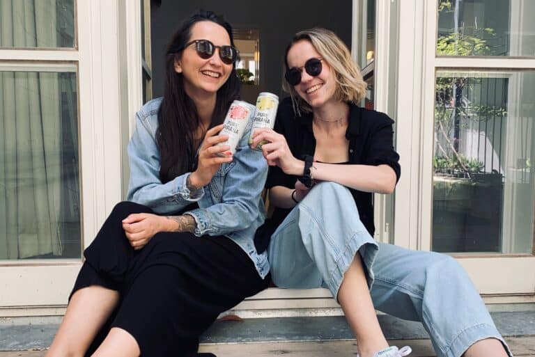Zwei Frauen sitzen auf einer Stufe und halten Pure Piraña Hard Seltzer Dosen