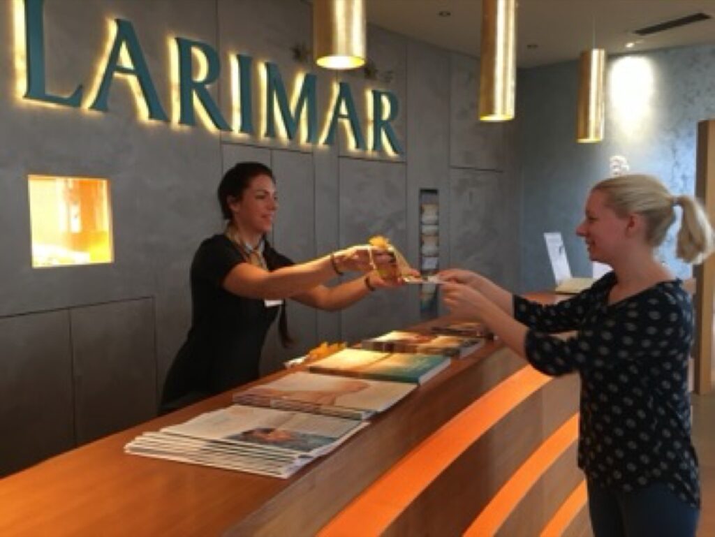 Gast erhält an der Wellnesshotel-Rezeption eine BI Good Produktprobe
