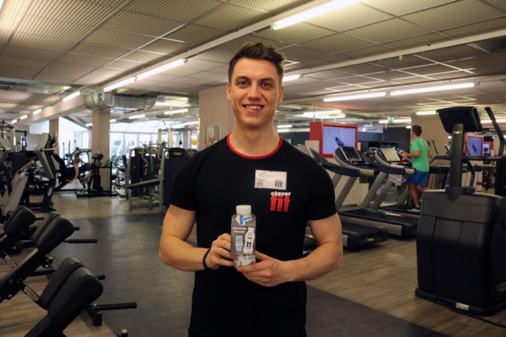 Trainer im Fitnessstudio mit einer NÖM Protein Produktprobe