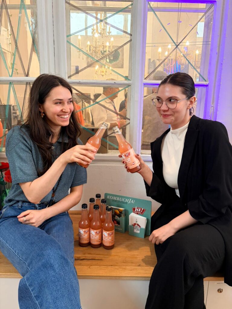 Zwei Berufstätige stoßen im Co-Working-Umfeld mit ja! Natürlich Raw Kombucha an, verteilt über Freudebringer