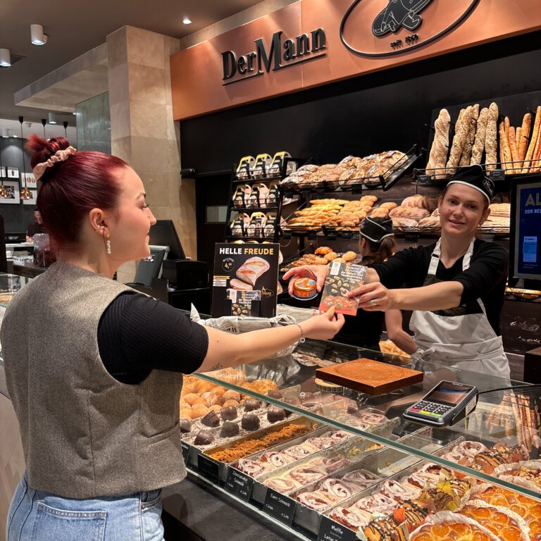 Übergabe einer Produktprobe an der Verkaufstheke einer Bäckerei