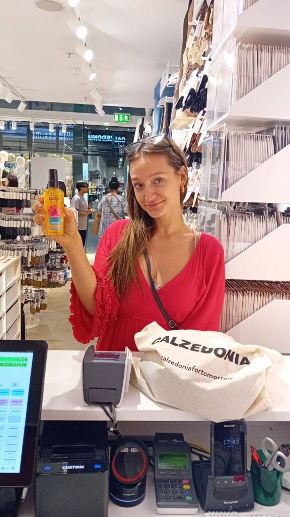 Frau in roter Bluse hält ein Produkt an der Kasse einer Drogerie